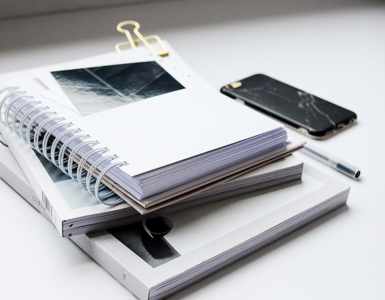 white spiral notebook beside black smartphone on white table