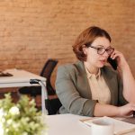 Photo of Woman Talking Through Smartphone While Using Laptop