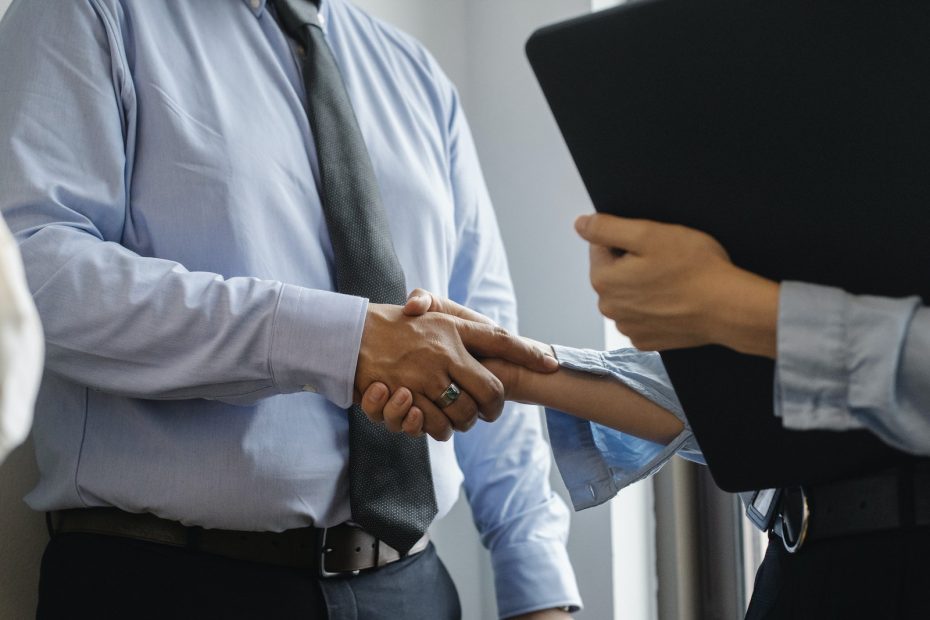 Crop anonymous man in formal shirt and tie shaking hand of woman with black folder while meeting in office
