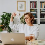 Woman Sitting in an Office in front of a Laptop and Waving Cash 