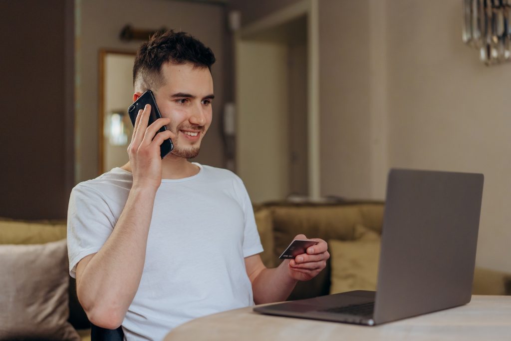 A Man Holding a Credit Card Using a Cellphone in Front of a Laptop