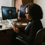 Curly Haired Woman in Front of a Computer Monitor Seriously Writing on a Paper