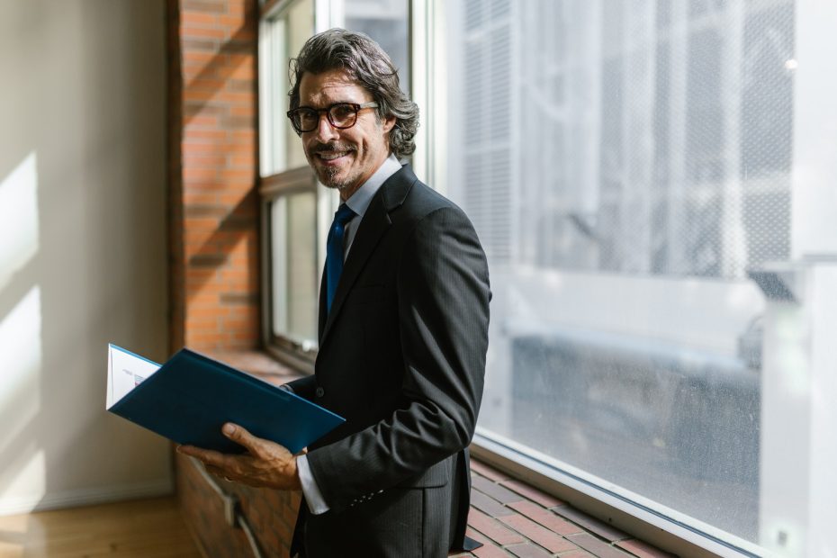 Smiling Man in Black Suit Holding a Blue Folder